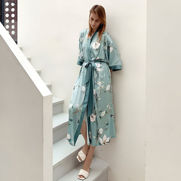 Femme portant un kimono bleu fleuri, noué à la taille. Vente de kimonos en ligne. Kimono long élégant avec motifs floraux. Boutique de vêtements japonais traditionnels et modernes.