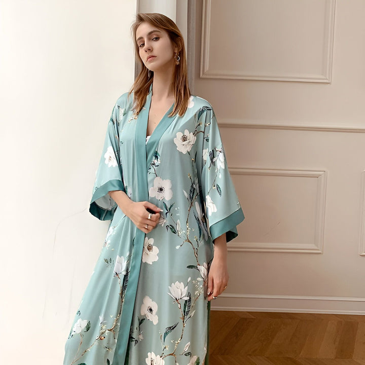 Femme portant un kimono long bleu clair à motifs floraux blancs. Kimono élégant et confortable, idéal pour la détente. Achetez nos kimonos de qualité supérieure en ligne.