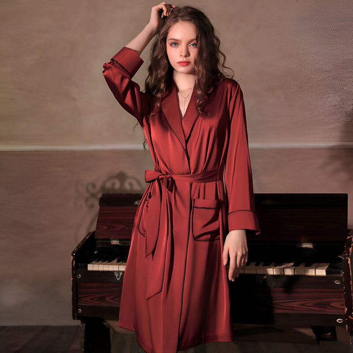Femme portant un kimono rouge bordeaux en satin avec ceinture, manches longues et poches. Élégant vêtement de détente, idéal comme peignoir ou robe de chambre. Vente de kimonos en ligne.