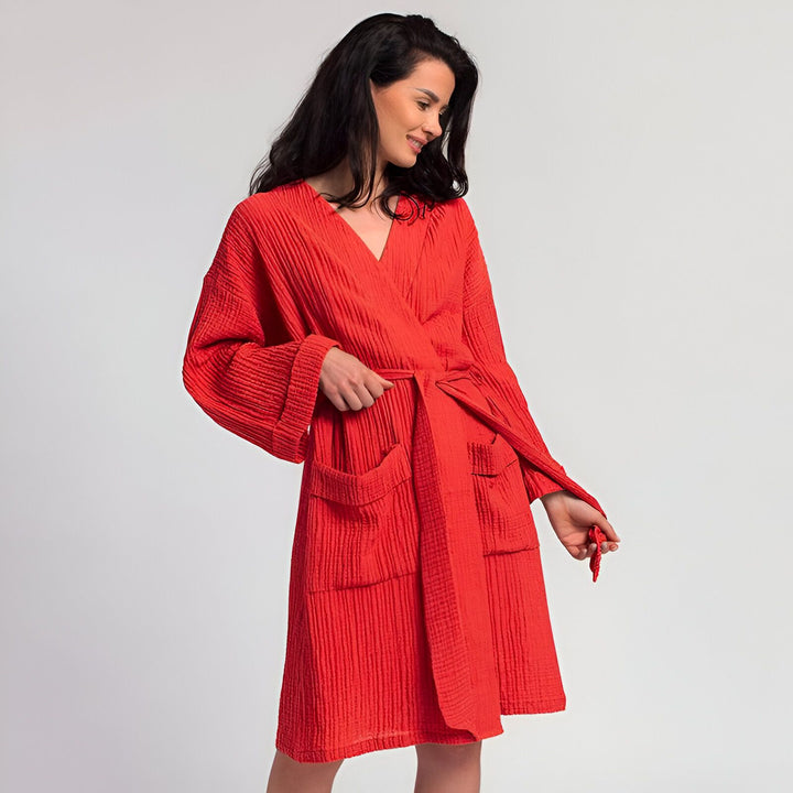 Femme souriante portant un kimono rouge avec ceinture. Peignoir confortable à manches longues et poches. Vêtements de détente élégants. Boutique de kimonos en ligne.