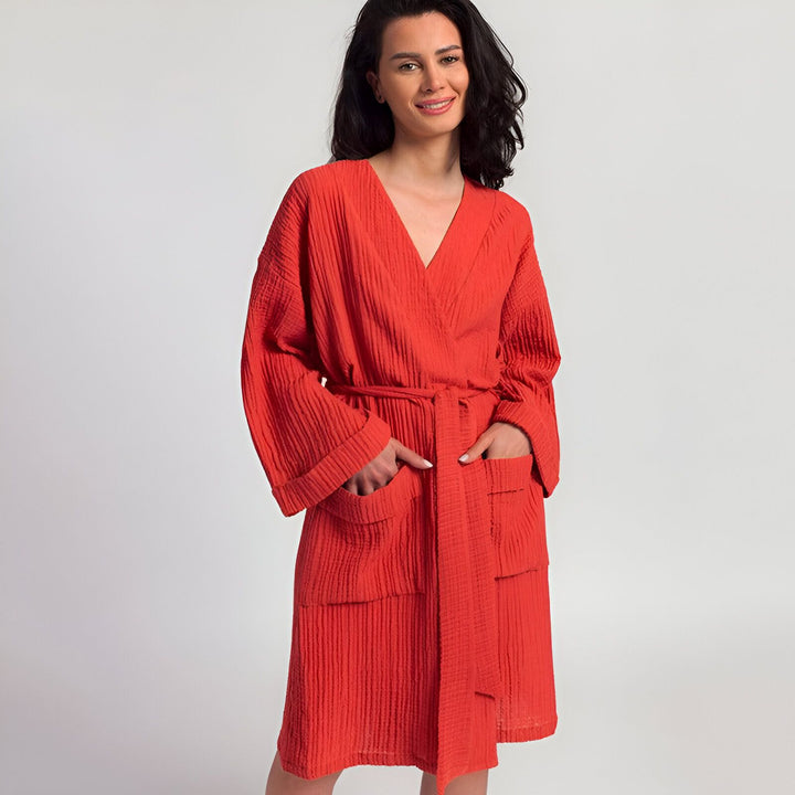 Femme souriante portant un kimono rouge texturé avec ceinture, mains dans les poches. Vente de kimonos confortables.