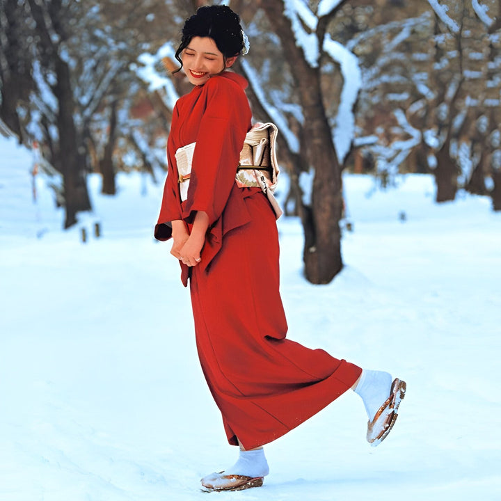 Femme souriante en kimono rouge traditionnel dans la neige. Vente de kimonos authentiques japonais. Élégance et charme intemporels. Découvrez notre collection de kimonos uniques.