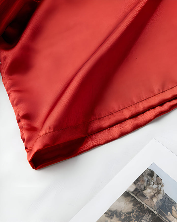 Détail de tissu rouge soyeux, possiblement un kimono. Découvrez notre collection de kimonos élégants. Tissu fluide et luxueux.