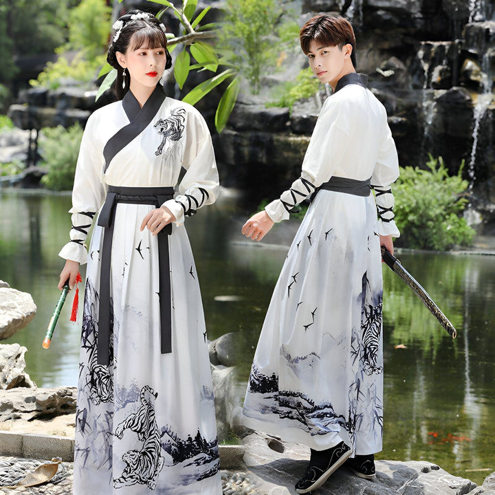 Image d'un couple en costumes traditionnels chinois blancs avec des motifs de tigres et d'oiseaux noirs, posant devant un étang avec une cascade. La femme tient une flûte, l'homme une épée.