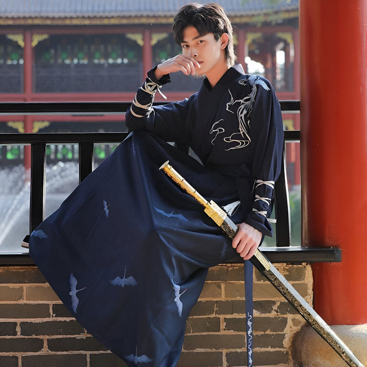 Un jeune homme en costume traditionnel chinois bleu marine, assis, tenant une épée ornée devant un bâtiment de style asiatique. Détails complexes sur le vêtement et l'épée.