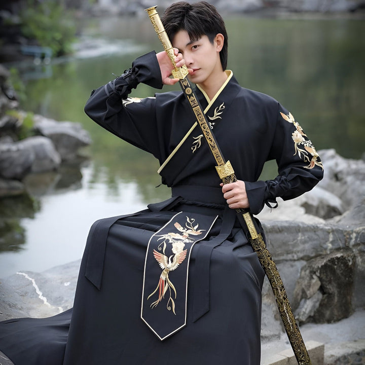 Jeune homme en tenue traditionnelle chinoise noire, broderies dorées, tenant une épée ornée près d'un lac. Style asiatique, élégance et tradition. Kimono moderne.