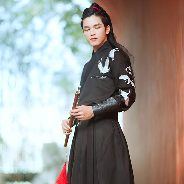 Homme portant un kimono noir brodé de grues, tenant une flûte. Vêtements traditionnels japonais en vente.