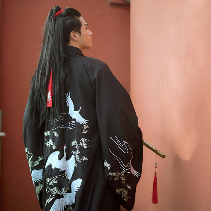 Homme portant un kimono noir brodé de grues blanches. Vêtement traditionnel japonais, disponible dans notre boutique.