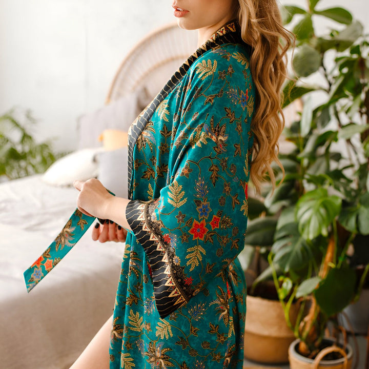 Femme portant un kimono turquoise à motifs floraux dans une chambre lumineuse. Détails du tissu et du design élégant. Découvrez notre collection de kimonos uniques.