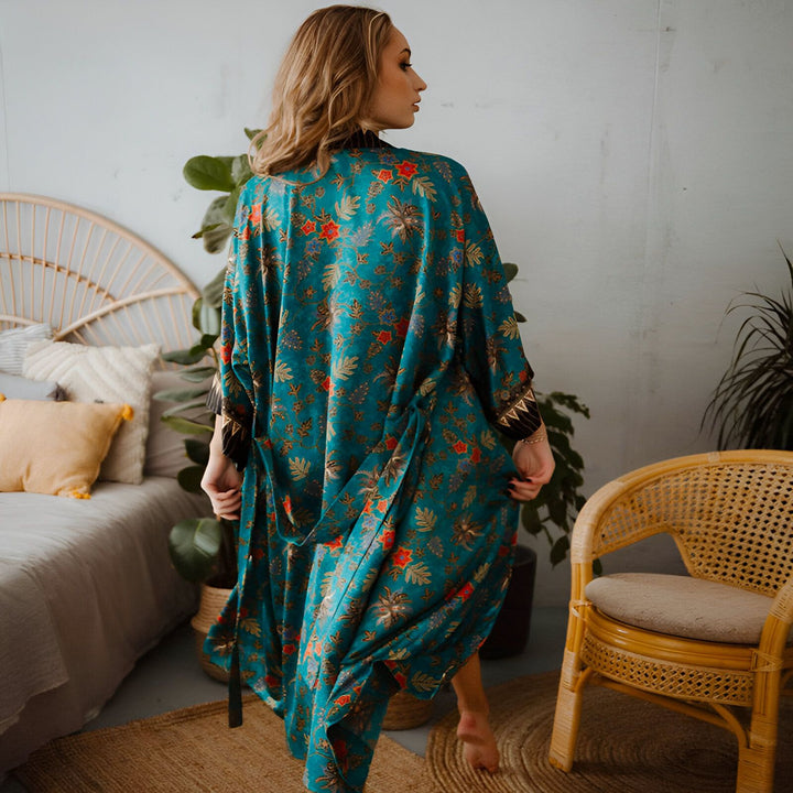 Femme portant un kimono bleu turquoise à motifs floraux dans une chambre bohème. Kimonos pour femmes disponibles à l'achat.