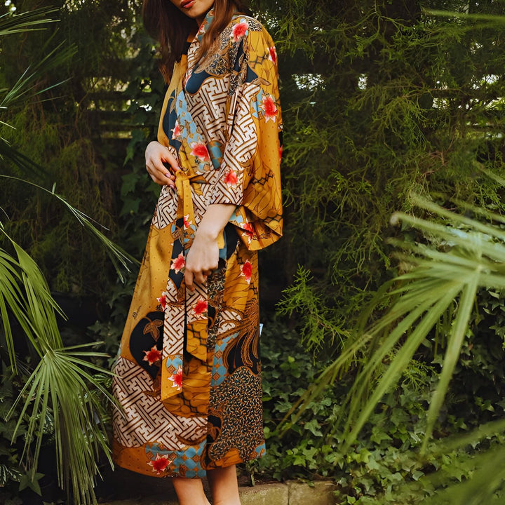 Femme portant un kimono jaune à motifs floraux et géométriques dans un jardin luxuriant. Kimonos élégants pour toutes occasions. Découvrez notre collection unique de kimonos.