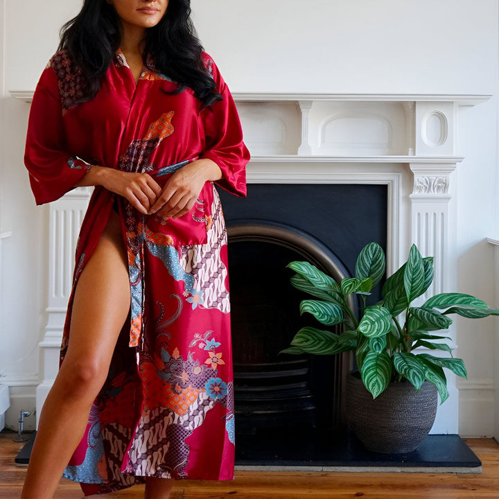 Femme portant un kimono rouge imprimé de motifs floraux et géométriques devant une cheminée. Kimonos de notre collection en vente en ligne.