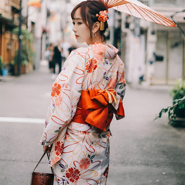 Femme portant un kimono fleuri blanc et orange, avec une ombrelle et un obi rouge. Vêtements traditionnels japonais, style kimono, vente de kimonos en ligne.