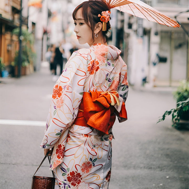 Femme portant un kimono fleuri blanc et orange, avec une ombrelle et un obi rouge. Vêtements traditionnels japonais, style kimono, vente de kimonos en ligne.