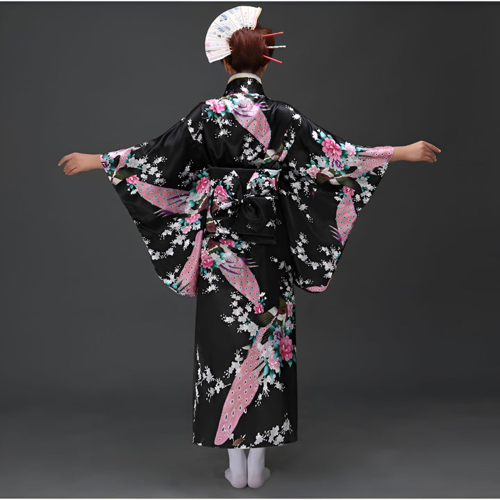 Kimono noir avec motifs de paons et de fleurs roses, porté avec un obi noir. Coiffure traditionnelle avec éventail et épingles rouges. Vêtements japonais traditionnels à vendre.