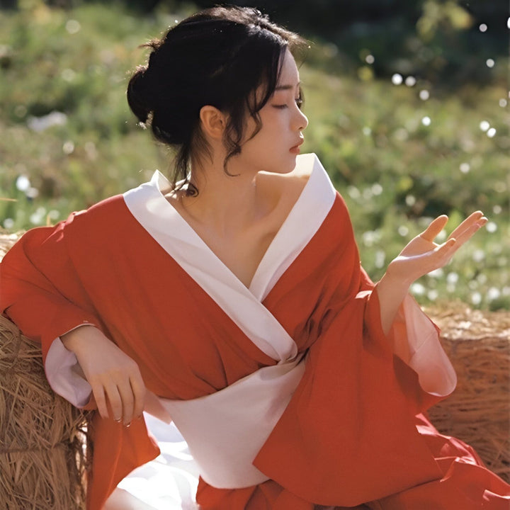 Femme asiatique portant un kimono rouge et blanc, assise dans un champ. Vêtements traditionnels japonais à vendre.