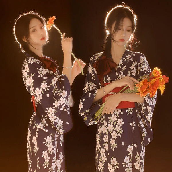 Deux femmes élégantes en kimonos traditionnels à motifs floraux, avec des ceintures rouges, tenant des fleurs. Découvrez notre collection de kimonos uniques.