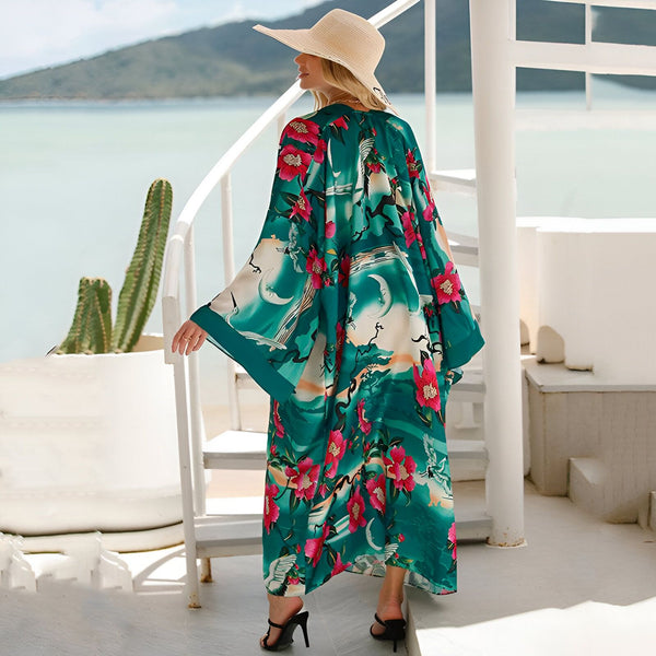 Femme portant un kimono long imprimé floral et paysage, chapeau de paille, sur une terrasse avec vue sur la mer. Kimonos de notre collection à découvrir.