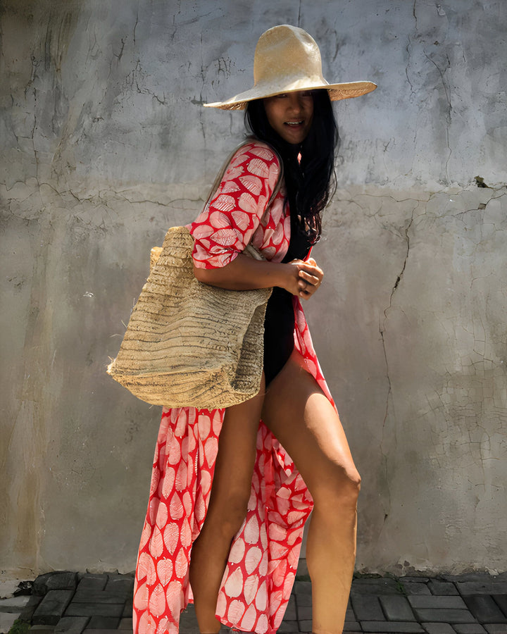 Femme souriante portant un kimono rouge à motifs, un chapeau de paille et un sac en fibres naturelles. Style estival et décontracté. Vêtements kimono à la mode.
