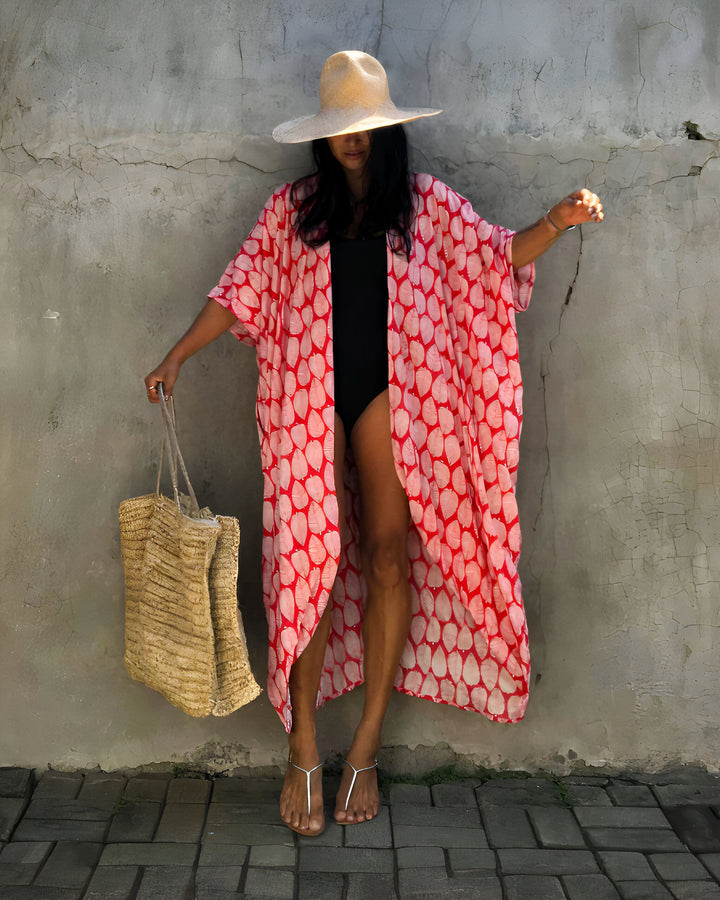 Femme portant un kimono rouge et blanc à motifs, un maillot de bain noir, un chapeau de paille et un sac en paille. Vêtements de plage, mode estivale, kimono de notre collection.