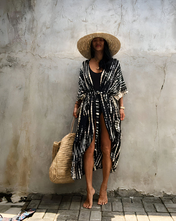 Femme portant un kimono noir et blanc avec un chapeau de paille, un maillot de bain noir et un sac en paille. Parfait pour la plage ou la piscine. Découvrez notre collection de kimonos uniques!