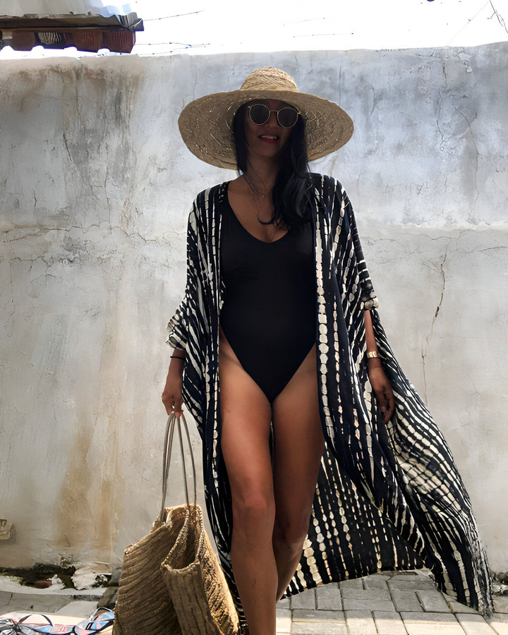Femme portant un kimono noir et blanc, maillot de bain noir, chapeau de paille et lunettes de soleil. Sac de plage en paille à la main. Mode kimono, vêtements de plage.