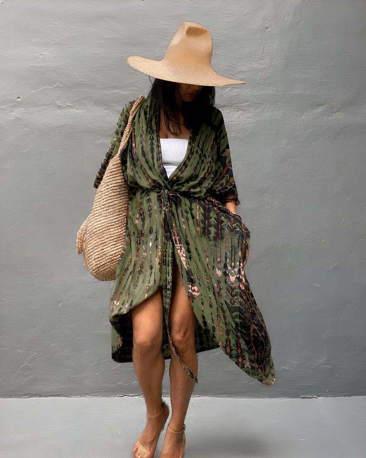 Femme portant un kimono vert à motifs, un chapeau de paille et un sac de plage en osier. Style bohème et décontracté. Vente de kimonos en ligne.