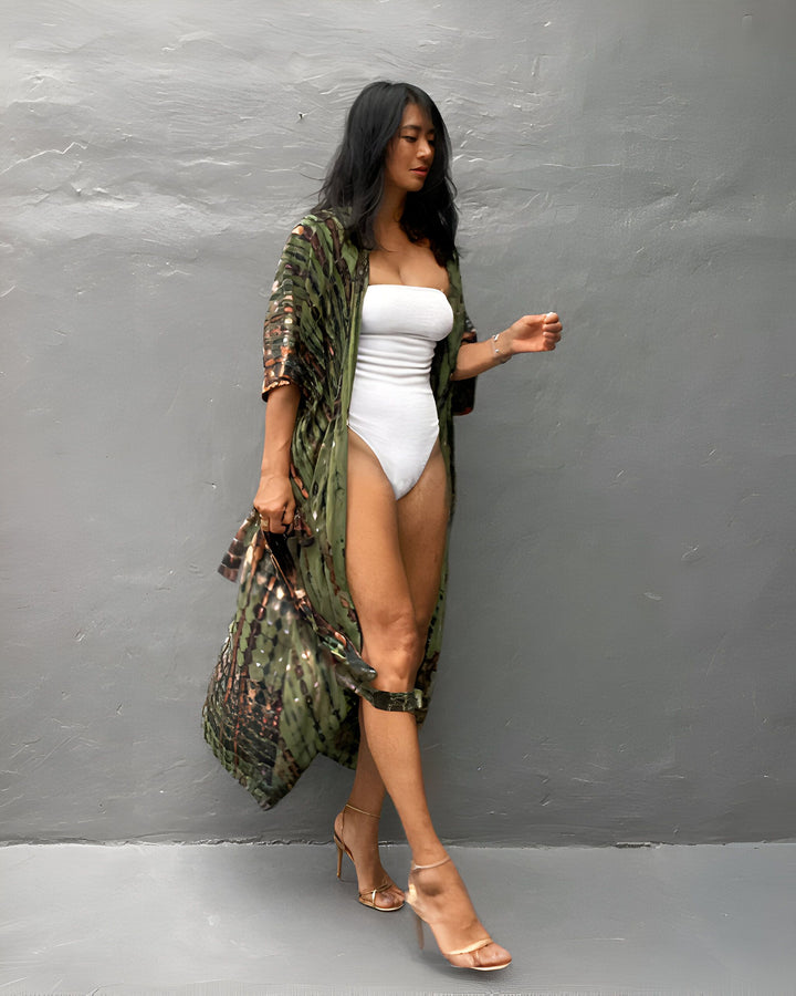 Femme portant un kimono long vert à motifs, maillot de bain blanc et talons hauts dorés. Style décontracté et élégant. Collection de kimonos pour femmes. Mode estivale.