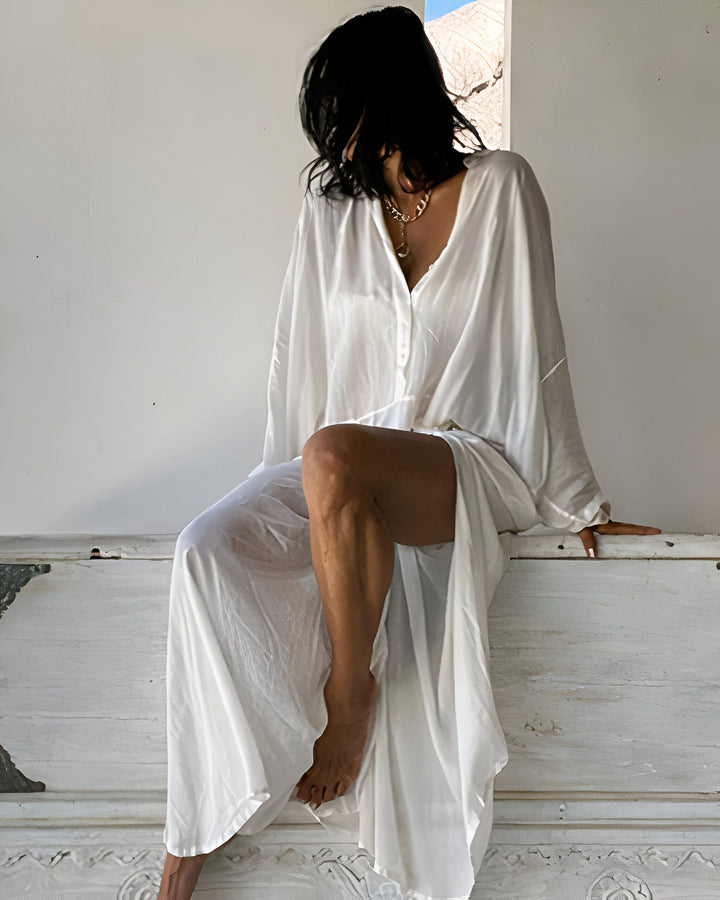 Femme portant un kimono blanc fluide, assise sur une malle ancienne. Vêtements de détente élégants, parfait pour la maison ou la plage. Découvrez notre collection de kimonos uniques.