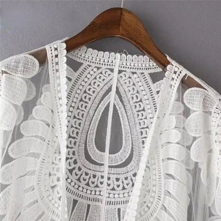 Kimono blanc en dentelle délicate sur cintre en bois. Détail de la broderie florale et géométrique. Vêtement léger et aéré, parfait pour l'été. Collection de kimonos pour femmes.
