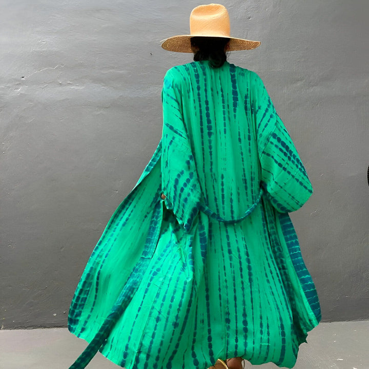 Femme vue de dos portant un kimono vert à motifs tie-dye bleus et un chapeau de paille. Vêtement d'extérieur ample et fluide, idéal pour la superposition. Collection de kimonos élégants.