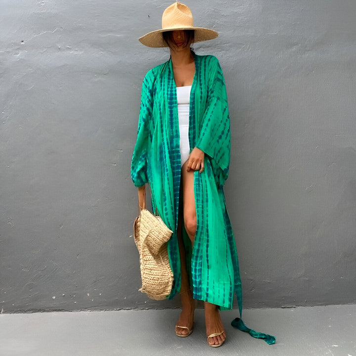 Femme portant un kimono long vert et bleu tie-dye, chapeau de paille et sac en paille. Kimonos pour femmes, vêtements de plage, robes d'été. Boutique en ligne de kimonos de qualité.