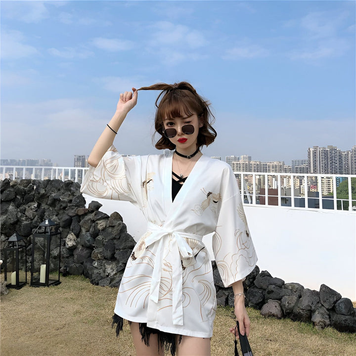 Femme portant un kimono blanc imprimé de grues dorées. Kimono ceinturé, style décontracté. Vêtements japonais à la mode. Découvrez notre collection de kimonos.