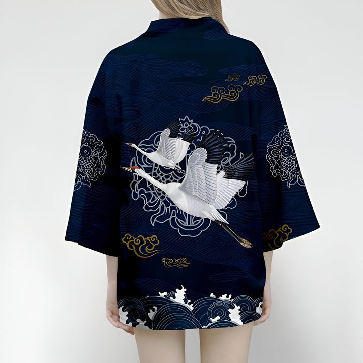 Dos d'une femme portant un kimono bleu marine avec des motifs de grues blanches en vol, des vagues et des nuages dorés. Kimonos pour femmes disponibles à l'achat.