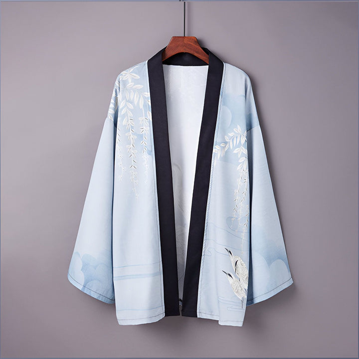 Kimono bleu clair avec motifs de grues et de feuilles, suspendu sur un cintre. Vêtement traditionnel japonais, idéal pour un style élégant et décontracté.