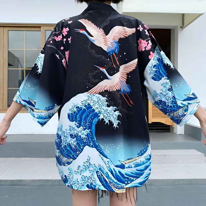 Dos d'une personne portant un kimono noir orné de motifs japonais : grues blanches, vagues bleues et fleurs de cerisier roses. Vente de kimonos.