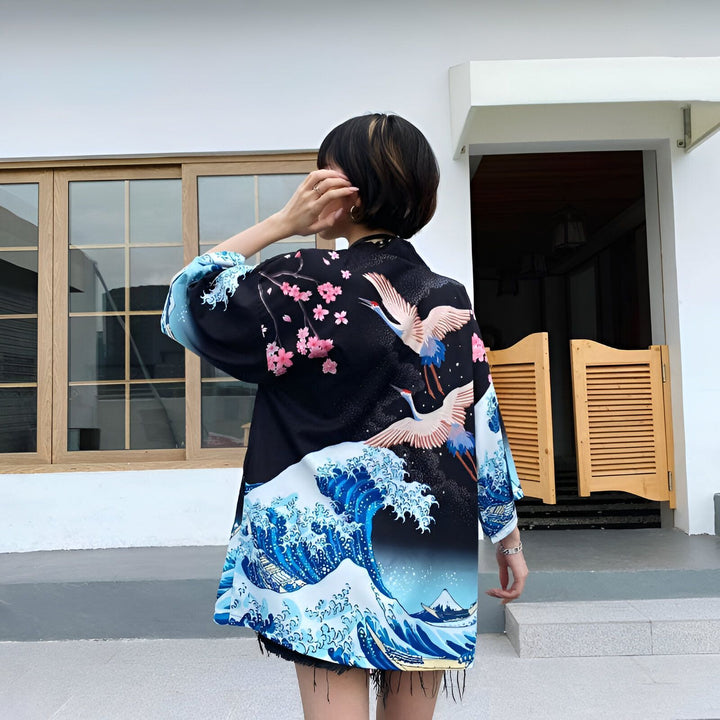Femme portant un kimono noir avec motifs japonais (vagues, fleurs de cerisier, grues). Kimono de style japonais, disponible à l'achat.