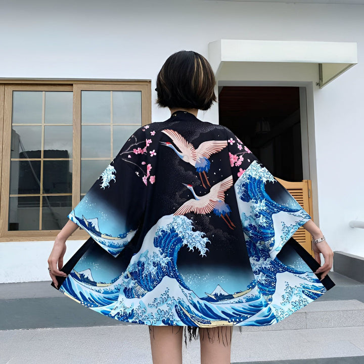 Vue arrière d'une femme portant un kimono noir avec des motifs de vagues bleues, de grues blanches et de fleurs de cerisier roses. Kimono de style japonais.