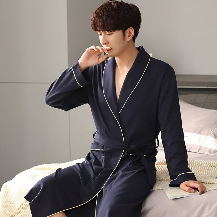 Homme portant un kimono bleu marine avec bordure blanche, assis sur un lit. Vente de kimonos.