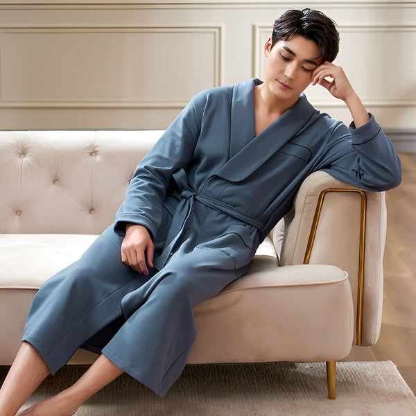 Homme asiatique détendu en kimono bleu sur un canapé beige. Vente de kimonos confortables pour hommes. Peignoir style japonais élégant. Mode masculine détente à la maison.