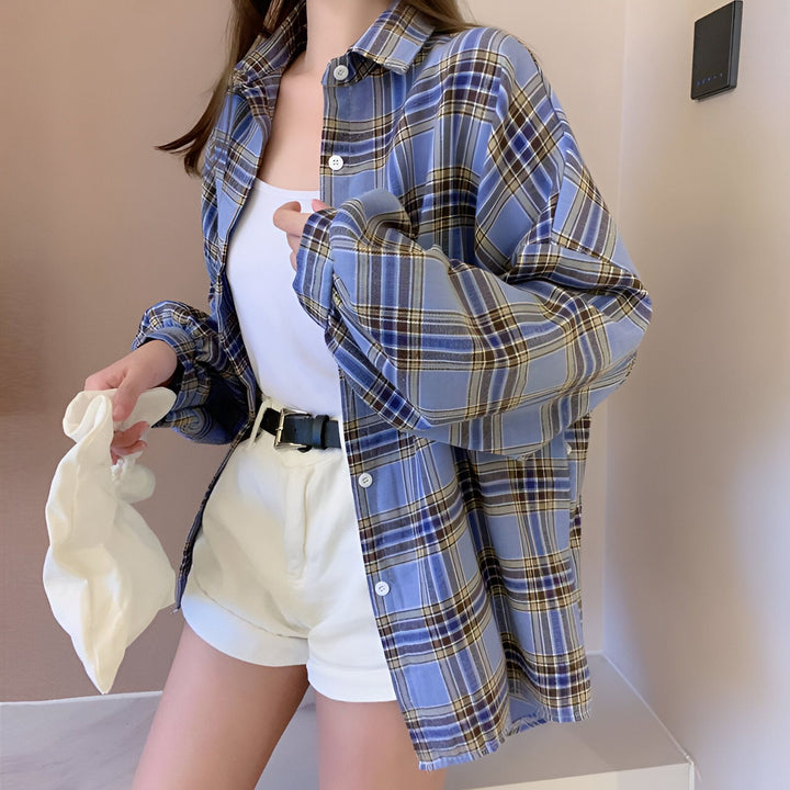 Femme portant une chemise kimono à carreaux bleue et blanche, sur un débardeur blanc et un short blanc avec une ceinture noire. Style décontracté et tendance.