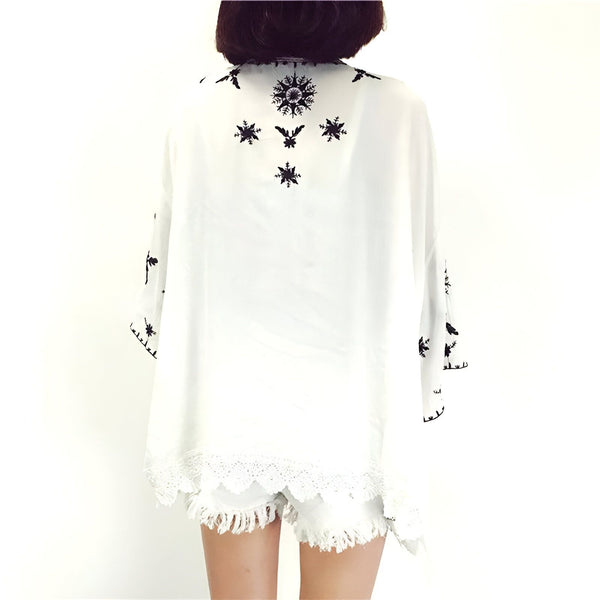 Vue arrière d'un kimono blanc avec broderies noires et bordure en dentelle. Vêtement ample et léger, parfait pour un style décontracté. Découvrez notre collection de kimonos uniques et tendance.
