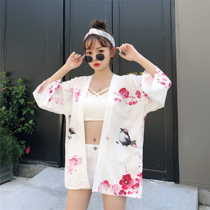 Jeune femme portant un kimono blanc à motifs floraux roses et oiseaux. Accessoires : lunettes de soleil et bandeau. Kimonos pour femmes disponibles à l'achat.