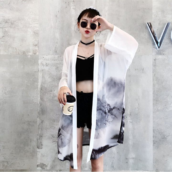 Femme portant un kimono blanc transparent avec motif de paysage, lunettes de soleil rondes, haut court noir et short. Kimono tendance pour femmes, disponible à l'achat.