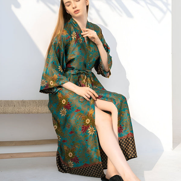Femme portant un kimono long et fleuri turquoise. Kimono avec ceinture, motifs floraux rouges et jaunes. Vêtements de détente confortables. Mode kimono.
