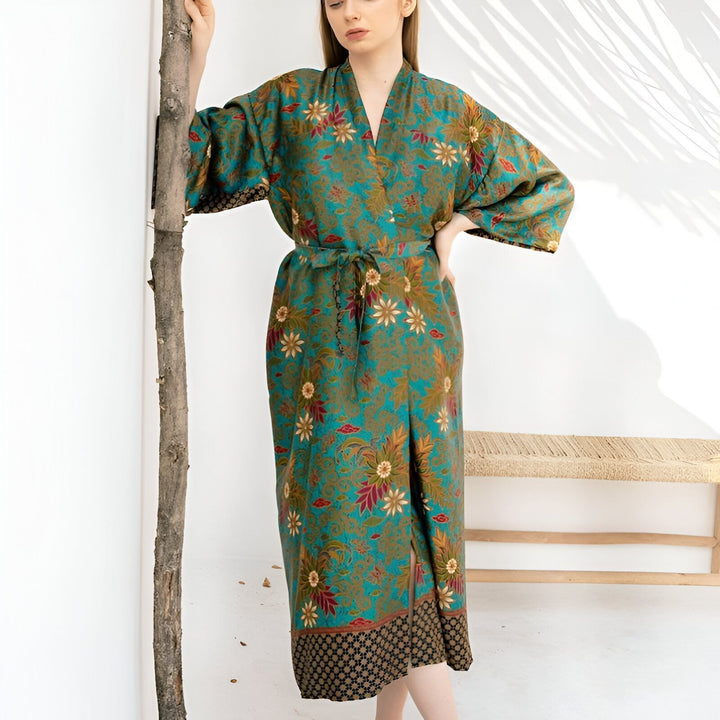 Femme portant un kimono long à motifs floraux turquoise et or. Ce kimono élégant est parfait pour la détente ou pour ajouter une touche d'exotisme à votre tenue. Découvrez notre collection de kimonos uniques.