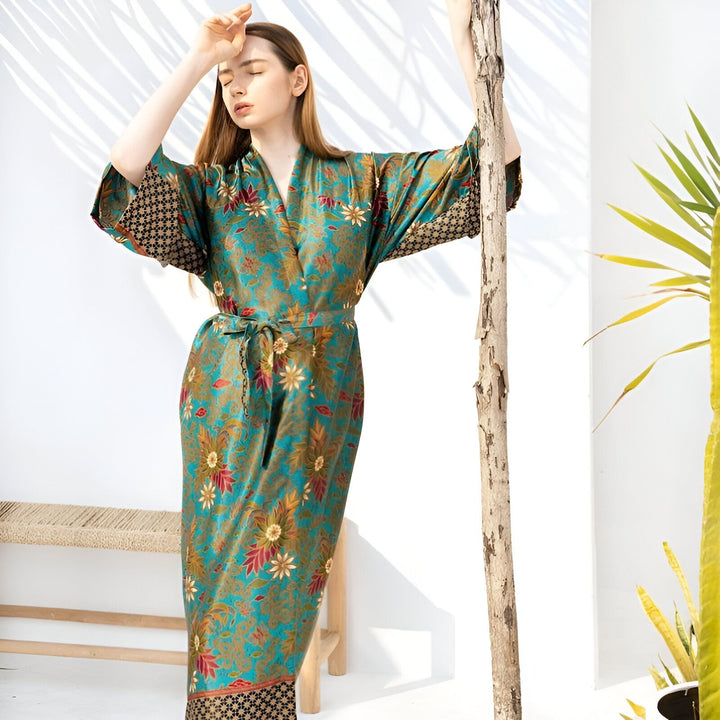 Femme portant un kimono long à motifs floraux turquoise et or, vendu dans notre boutique. Kimono de style traditionnel japonais avec ceinture. Vêtements d'intérieur élégants et confortables.