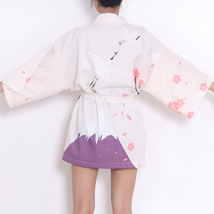 Kimono japonais blanc avec motifs de grues, fleurs de cerisier roses et montagne violette. Vêtement traditionnel élégant et confortable. Découvrez notre collection de kimonos uniques.