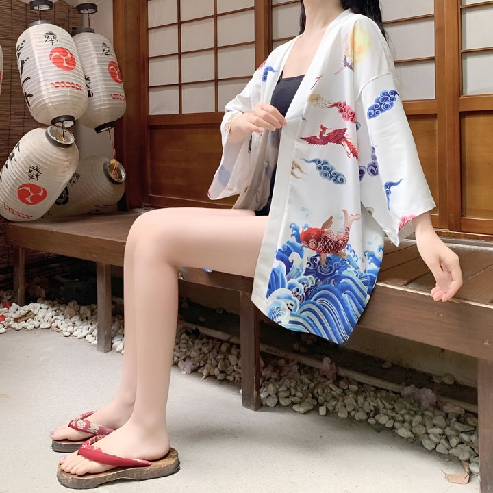 Femme assise portant un kimono blanc avec des motifs de carpe et de phénix. Lanternes japonaises traditionnelles en arrière-plan. Kimonos en vente.