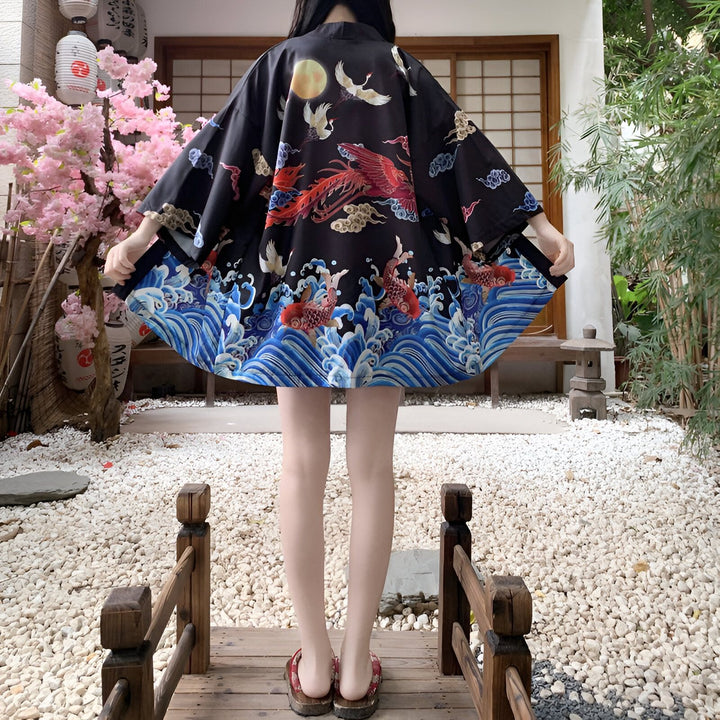 Femme portant un kimono noir orné de motifs japonais : phénix rouge, grues blanches, lune et vagues bleues avec des carpes. Kimono traditionnel disponible à l'achat.
